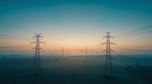 Serene view of electrical transmission towers and power lines silhouetted against a gradient sky transitioning from deep teal to warm amber at blue hour